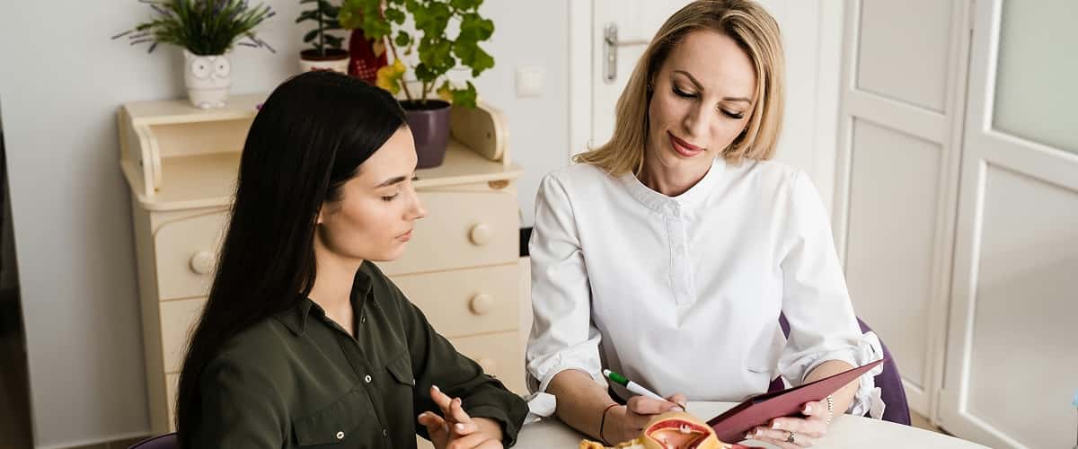 Två kvinnor samtalar vid ett bord. En skriver i en anteckningsbok.