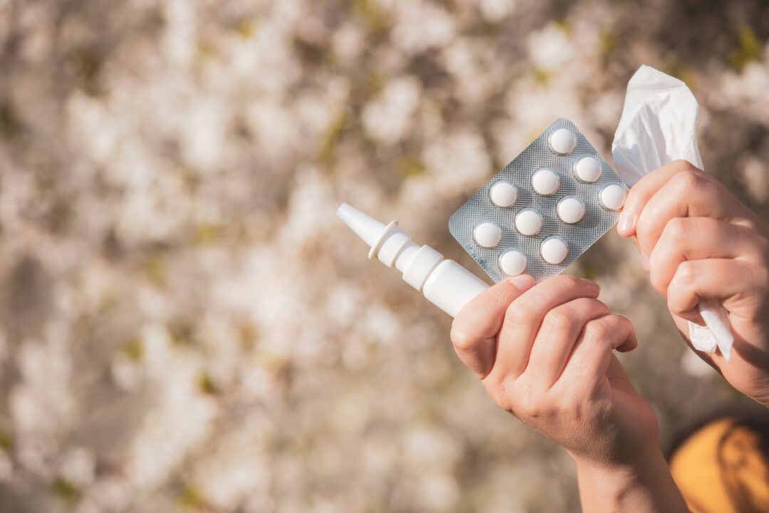 Händer som håller i nässpray, pollenmedicin och näsduk